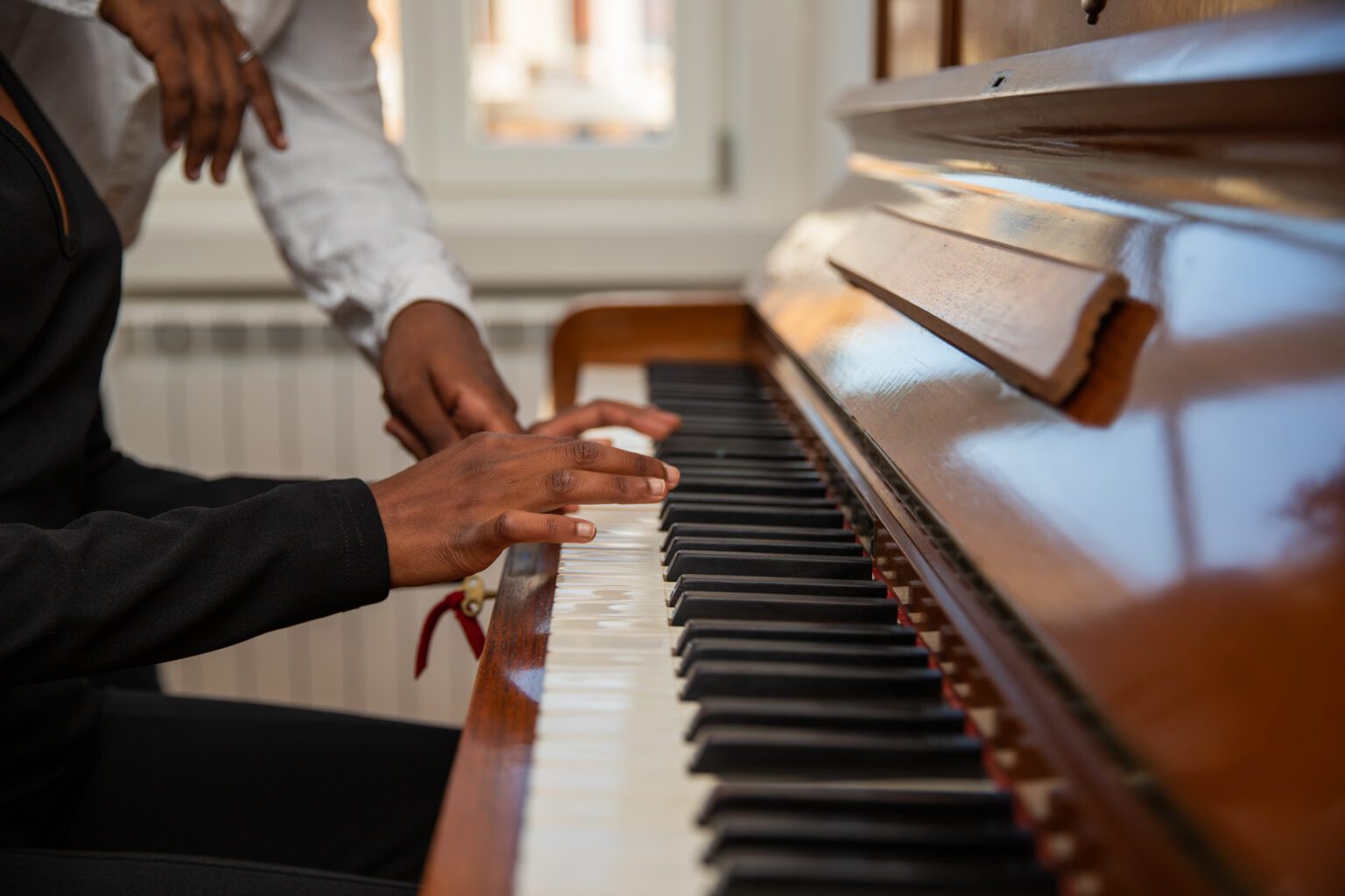 Close-up of the hands of a girl playing a piano together with a friend.